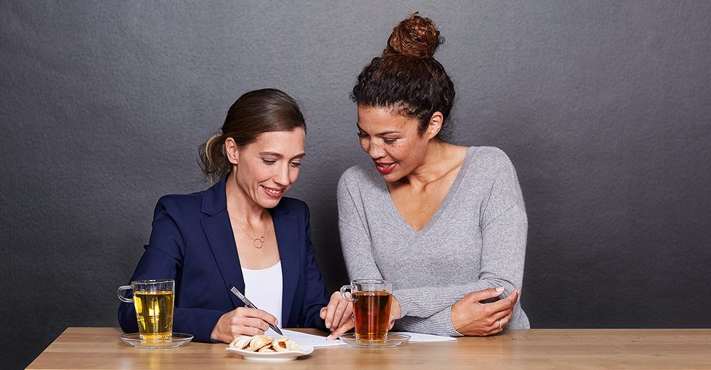 Zwei Frauen unterhalten sich bei einer Tasse Tee und Gebäck.