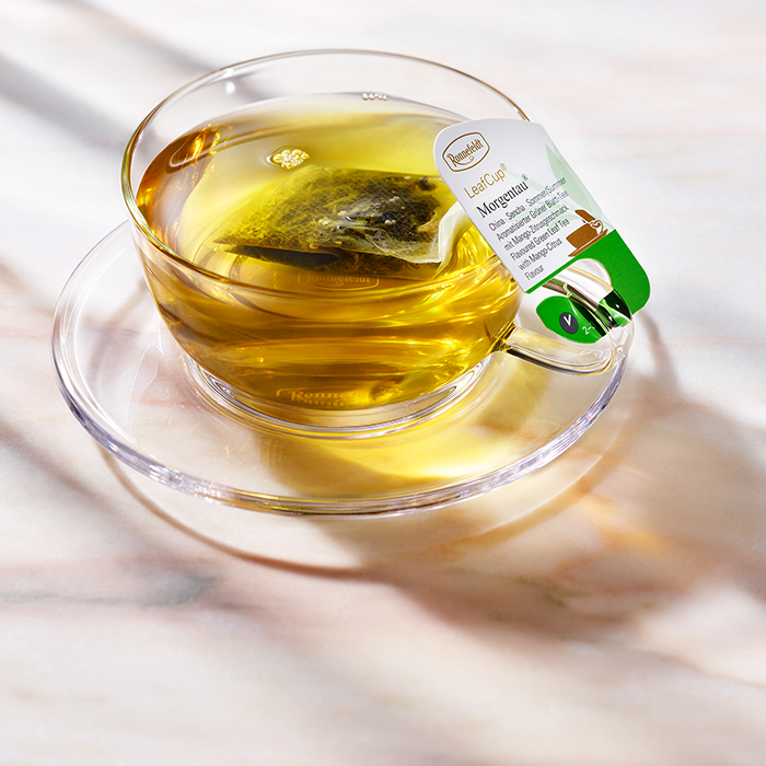 Glass cup of Ronnefeldt LeafCup® Morgentau® green tea with tag.