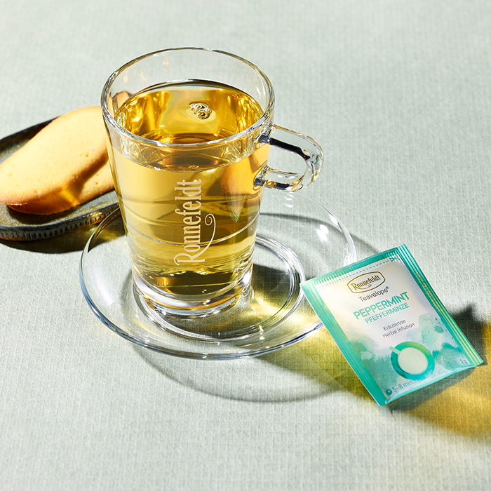 Glass cup of Ronnefeldt Teavelope® Peppermint tea with biscuits.