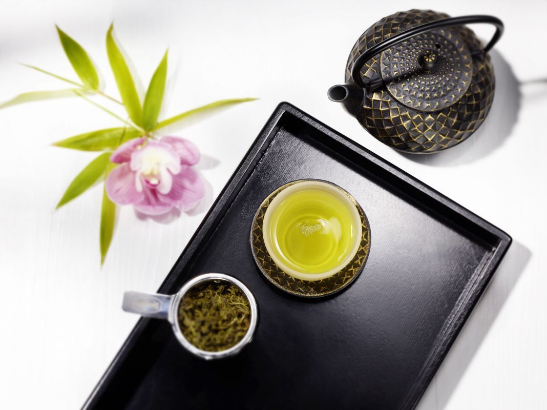 Teezeremonie mit gusseiserner Teekanne, Tasse grünem Tee auf Tablett, Teeblätter und Orchidee als Dekoration