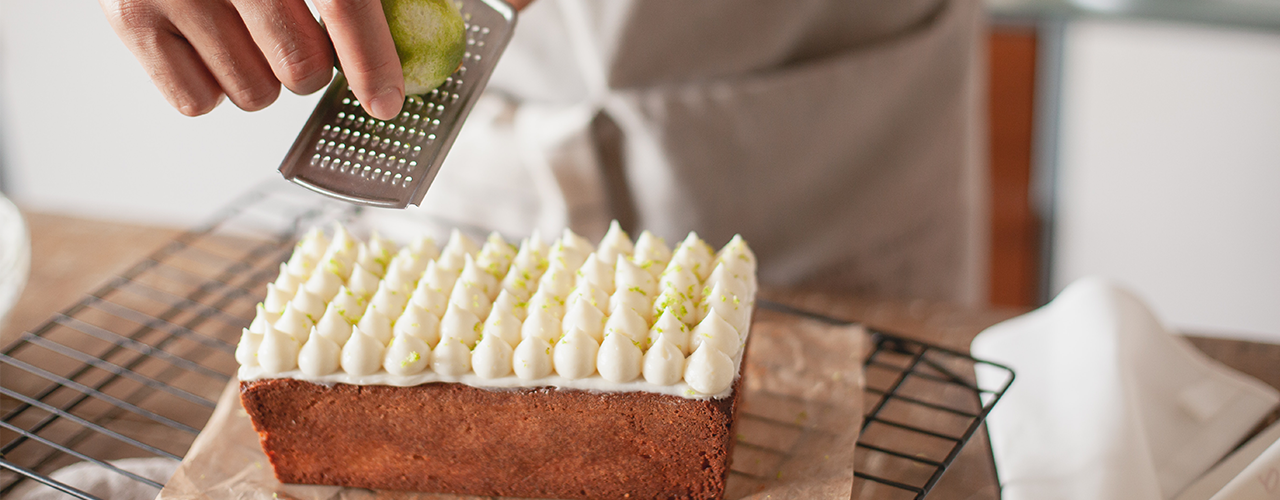 Zitronenkuchen mit Sahnetupfen wird frisch mit Limettenschale garniert