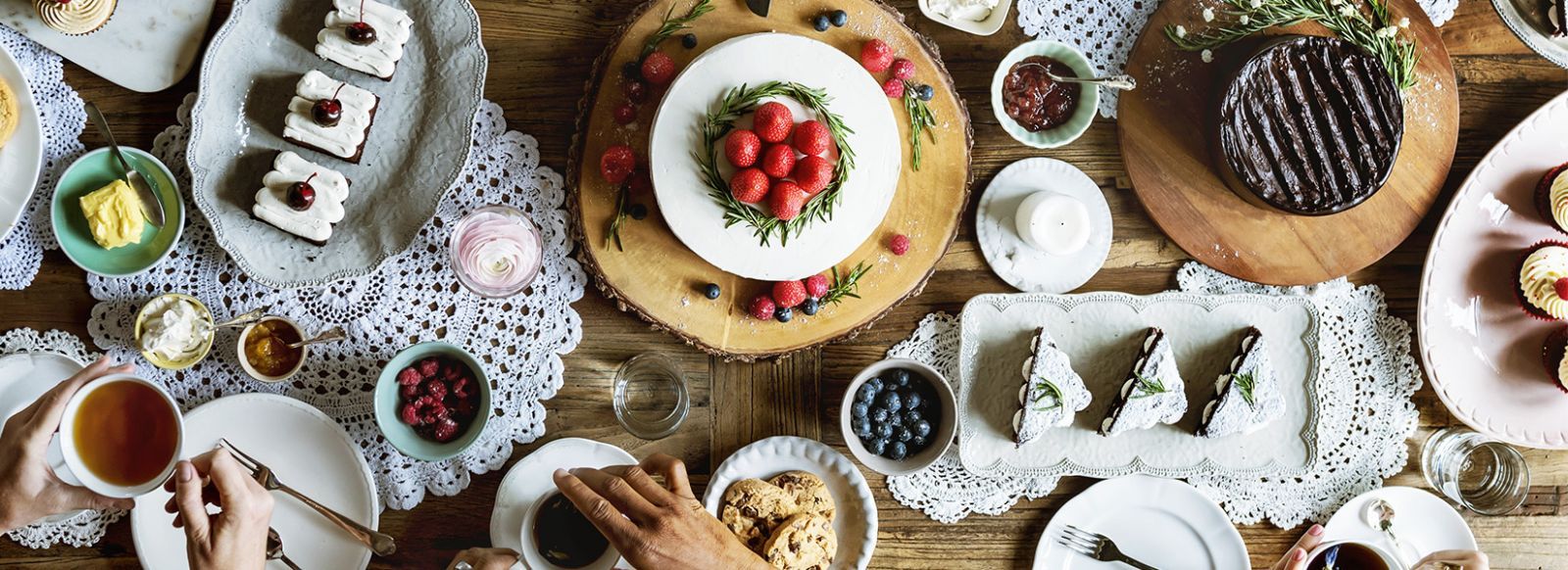 Festlich gedeckter Tisch mit Tee, Kuchen, Beeren und Gebäck auf Häkeldeckchen in gemütlicher Atmosphäre