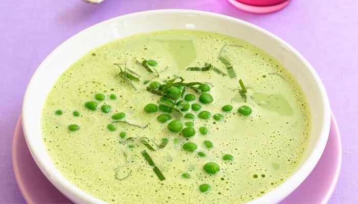 Cremige grüne Erbsensuppe, garniert mit frischen Erbsen und Kräutern