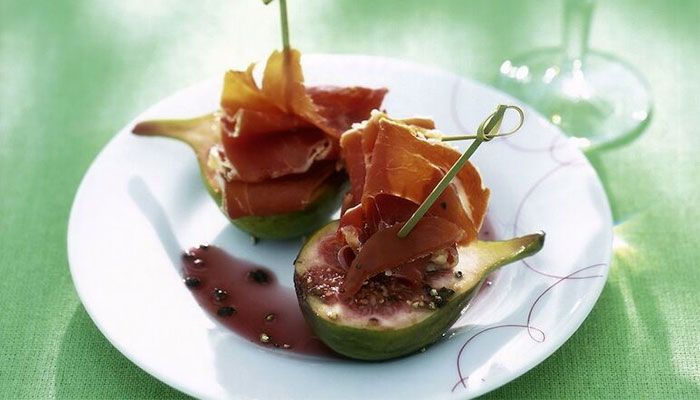 Halbierte Feigen mit Ziegenkäse und Parmaschinken auf einem weißen Teller