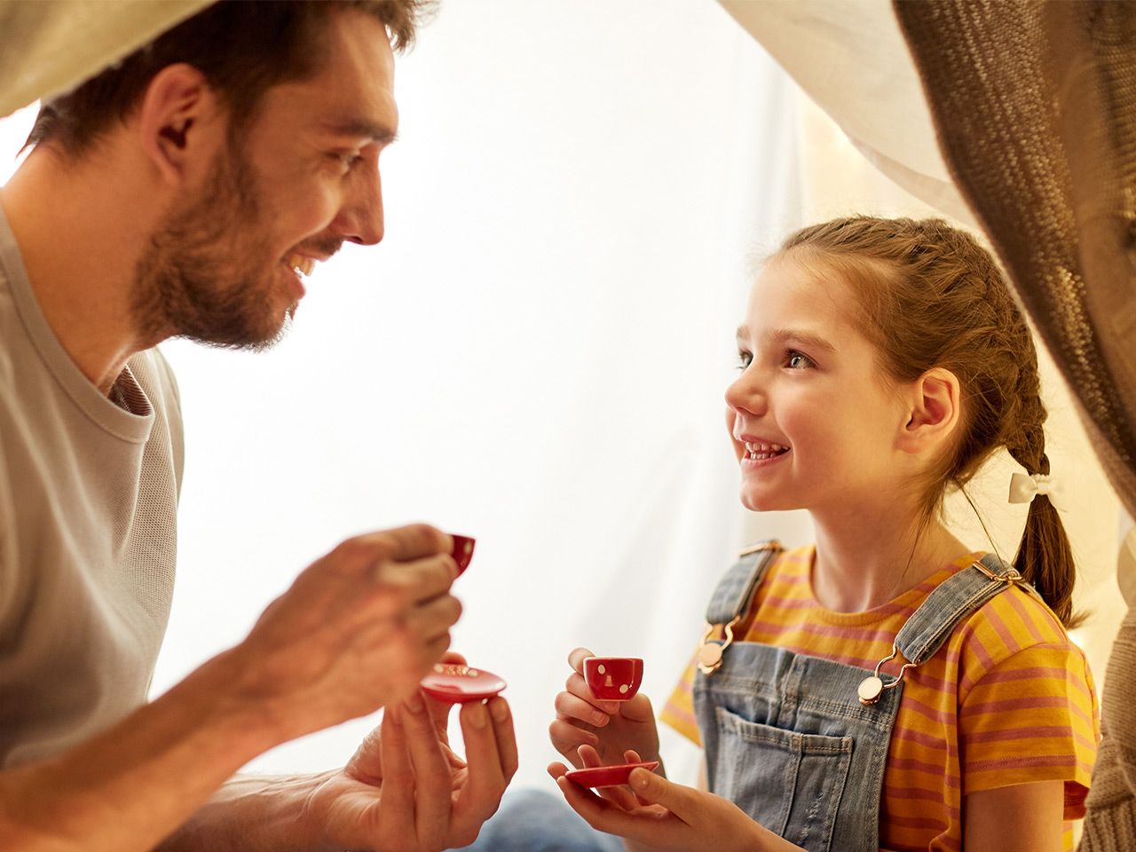 Vater und Tochter trinken lachend Tee aus kleinen Tassen