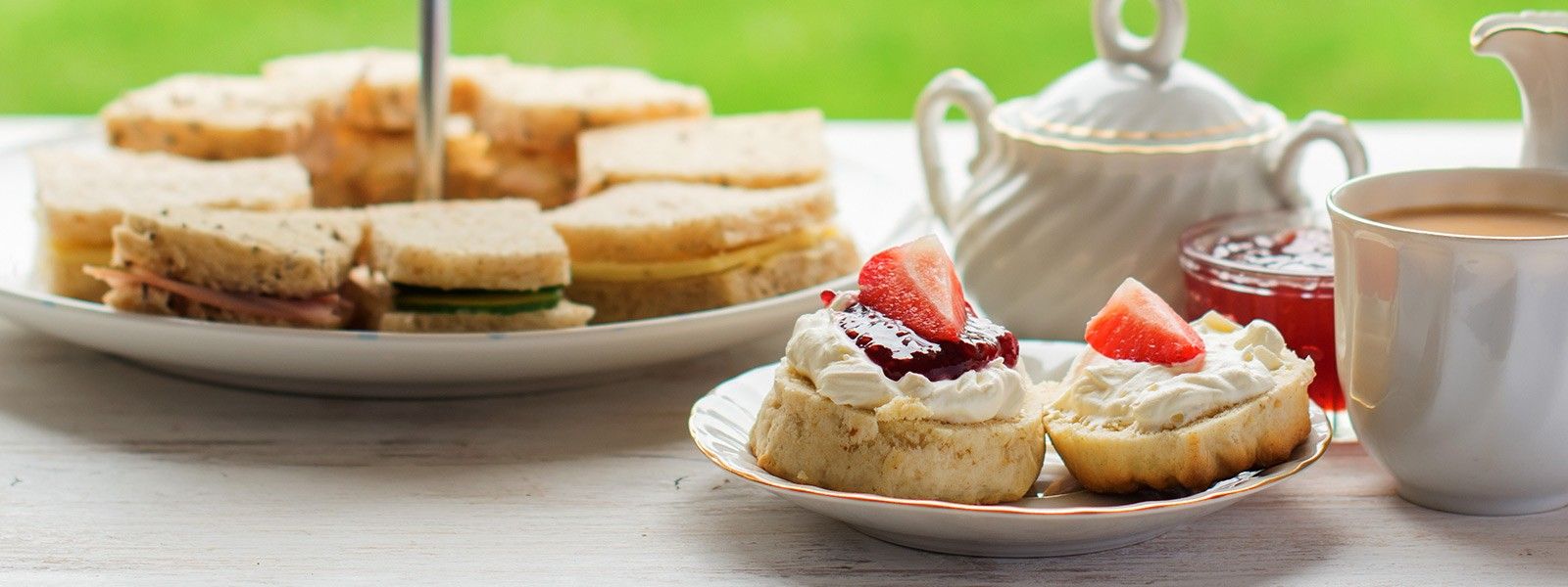 Traditionelle englische Teatime mit Scones, Clotted Cream, Erdbeermarmelade, Tee und Sandwiches auf weißem Tisch im Freien