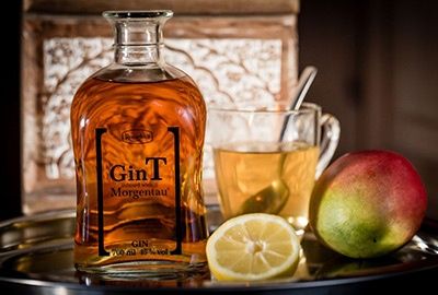 GinT neben Glastasse mit Tee, Zitrone und Mango