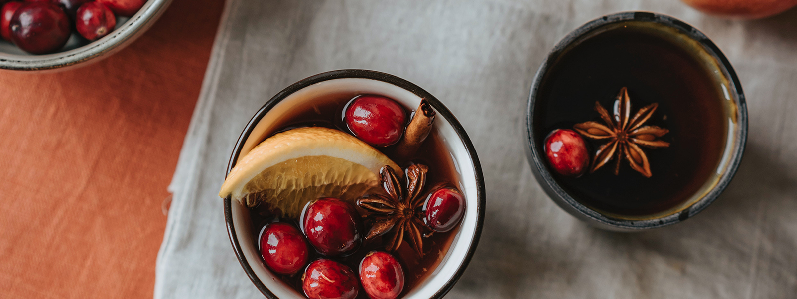 Tassen mit Tee, dekoriert mit Cranberries, Orangenscheibe, Sternanis und Zimtstange