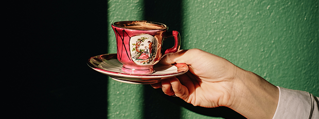 Hand hält rosa Vintage-Teetasse mit Untertasse vor grünem Hintergrund