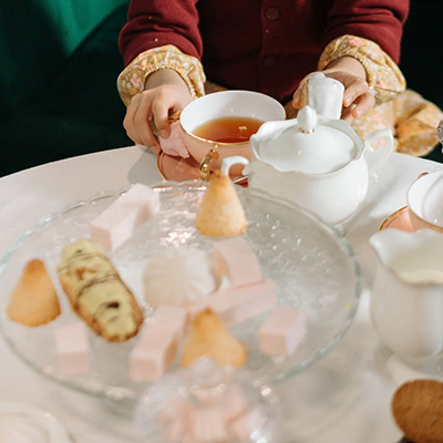 Teezeit mit weißem Porzellanservice und feinem Gebäck auf Glasplatte