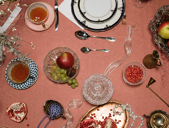 Festlich gedeckter Tisch mit Tee, Obst, Granatapfelkernen, edlem Geschirr und Dekoration auf rosafarbener Tischdecke