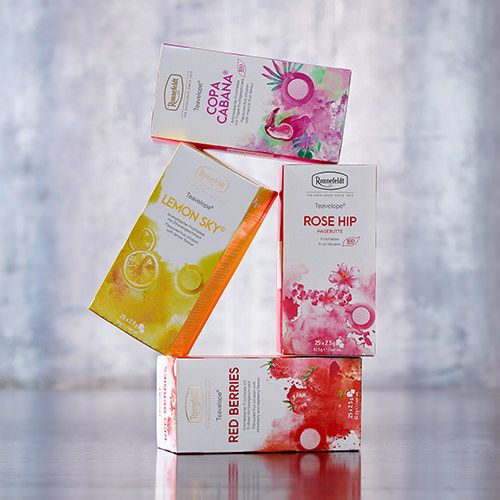 Vier Ronnefeldt Teavelope® Teepackungen in den Sorten Copa Cabana, Lemon Sky, Rose Hip und Red Berries, kunstvoll gestapelt vor einem dezenten Hintergrund.