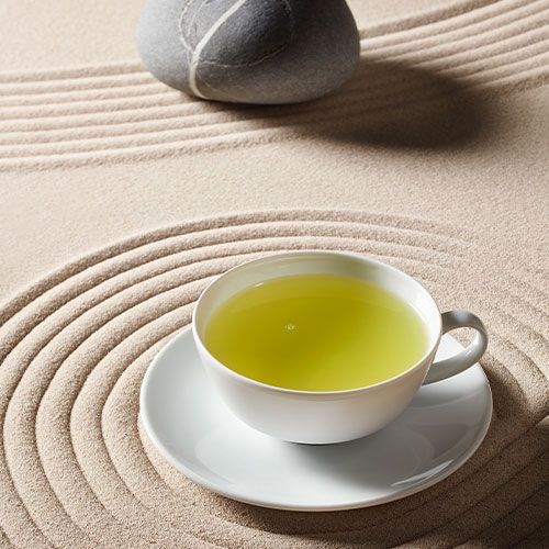 Weiße Teetasse mit weißem Tee auf einem sandigen Hintergrund mit harmonischen Kreisen, neben einem glatten Stein.